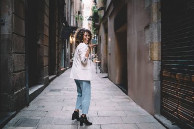 Tarz sahibi giyinmiş mutlu etnik kadın tarihi şehirde yürürken kameraya bakıp gülüyor.