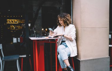 Modayı takip eden kadın tasarımcı projede çalışıyor ve yazlık terasta çağdaş restoranda zaman geçirirken aletler kullanıyor.