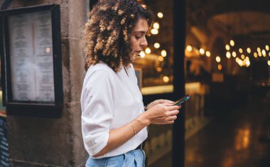 Kapıda duran akıllı telefonlu genç bir etnik kadının sokak ortasında dinlenirken sosyal medyada sohbet mesajlarına göz atması