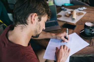 Gelişigüzel giyinen sakallı, tahta masada oturan ve yaratıcı iş yerinde uzak bir proje üzerinde çalışırken notlar yazan bir adamdan.