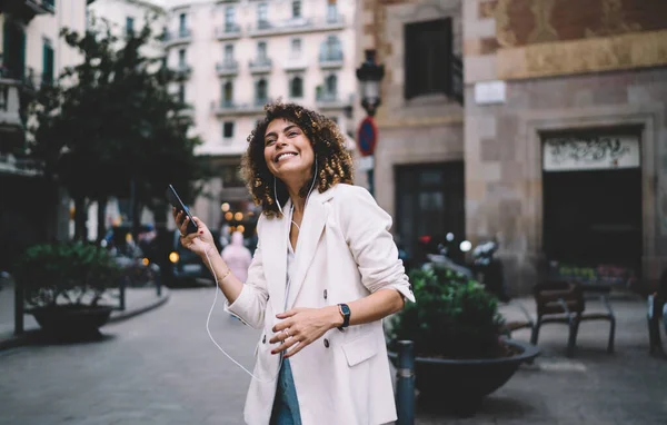 Młoda Uśmiechnięta Kobieta Kręconymi Włosami Szczęśliwie Słuchająca Muzyki Telefonie Komórkowym — Zdjęcie stockowe