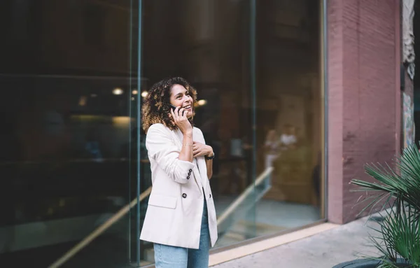 街を歩いている間に電話で笑いと感情的に話して離れて見て白いジャケットの陽気な民族のスタイリッシュな若い女性 — ストック写真