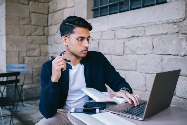 Konzentrierter Ethnischer Kerl Arbeitet Laptop Und Hält Stift Zum Schreiben — Stockfoto