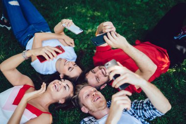 Bir grup neşeli hippi, piknik için toplanma sırasında dijital akıllı telefonlardan video bloğu izleyen neşeli erkek ve kadınlar için çevrimiçi mesajlaşma için cep telefonlarıyla parkta dinleniyor.