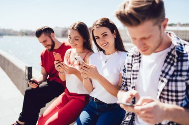 Neşeli bir kadının portresi, bluetooth 'a bağlı senkronize akıllı telefon cihazlarıyla online oyunlar oynayan beyaz tenli hippi adamlarla buluşmaktan keyif alıyor.