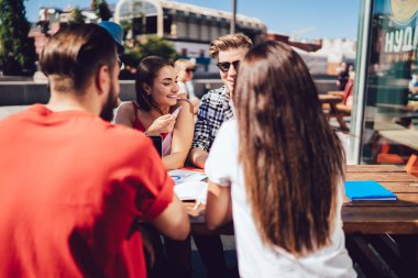 20 yaşındaki mutlu meslektaşlarım serbest çalışma üzerine arkadaşça beyin fırtınası toplantısının tadını çıkarıyorlar. Kaldırımdaki kafede gülümseyen neşeli insanlarla iş birliği yapıyorlar.