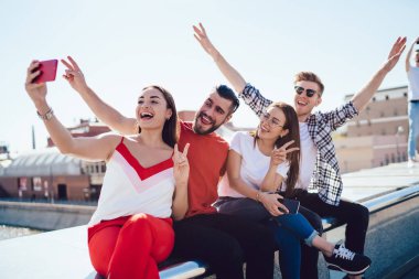 Neşeli erkek ve kadın en iyi arkadaşlar çatı katında eğleniyorlar arka planda şehirle selfie çekiyorlar, neşeli hipsterlar çifte randevu sırasında komik videolar çekiyorlar.