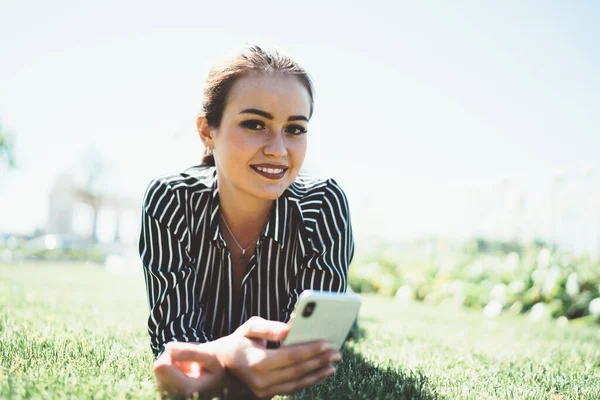 公園草の上に横たわる陽気なヒッピーの女の子の肖像とスマートフォンネットワーキングのための余暇時間の間にカメラで笑顔 週末の間にポーズ現代の携帯電話技術を持つ若い千年紀 — ストック写真