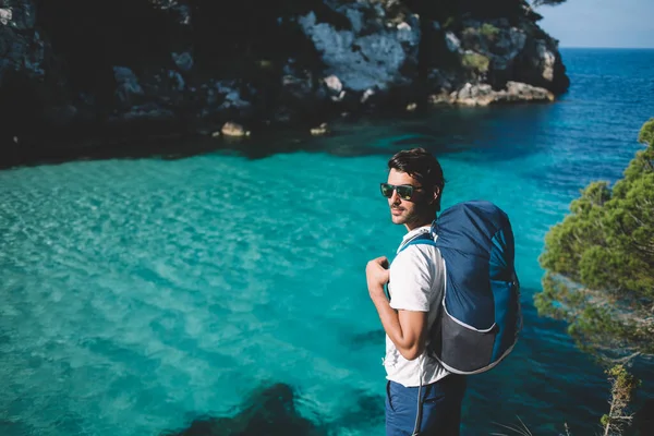 持太阳镜的南亚背包客带着背包游览阳光灿烂的西班牙和海岸线美丽的巴利阿里群岛 带着海湾探索野外自然环境 — 图库照片