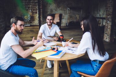 Gündelik hayattaki çok ırklı iş arkadaşları ahşap masada otururken ve birlikte çalışırken yaratıcı modern çalışma alanlarının çizelgelerini analiz ederken mutlu olurlar.