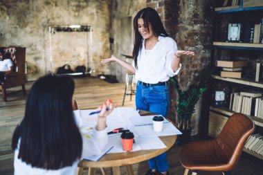 Gündelik giysiler içindeki kafası karışmış genç bayan meslektaşlar modern çatı katında çalışırken iş projeleri hakkında konuşuyorlar.