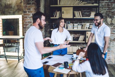 Gündelik giysiler içinde bir grup erkek ve kadın meslektaşlar modern iş yerinde iş raporları üzerinde çalışırken eğleniyorlar.