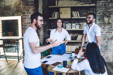 Meslektaşlar yeni projeyi tartıştıktan sonra ara veriyorlar ve büyük kitaplık ve ayna ile sıcak bir odada birlikte gülüp eğleniyorlar.