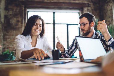 Mutlu iş arkadaşları gündelik giysiler içinde güler yüzlü ve çatı katındaki ahşap masada otururken birbirleriyle konuşurlar.