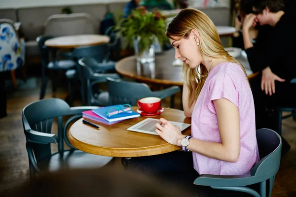現代的なカフェで仕事をしながら 木製のテーブルとブラウジングタブレットに座ってカジュアルな服装で焦点を当てた女性の側面図 — ストック写真