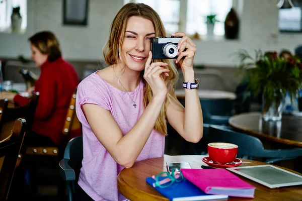 Позитивная Женщина Повседневной Одежде Улыбается Фотографируется Фотокамеру Сидя Деревянным Столом — стоковое фото