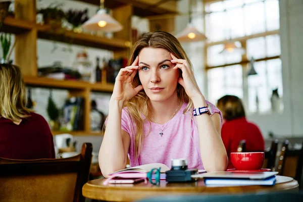 Concentrerende Vrouw Zitten Aan Houten Tafel Met Notitieblok Wrijven Tempels — Stockfoto