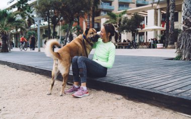 Mutlu Kafkasyalı fit kız, deniz kıyısındaki kardiyo antrenmanından sonra dinlenen, yürüyüş ve antrenman için boş zamanlarının tadını çıkaran beyaz köpekle eğleniyor.