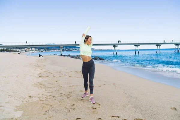 활발히 활동하는 운동하는 여자가 해변의 모래사장에서 시간을 파도를 구경하는 — 스톡 사진