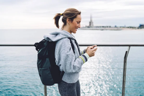 Widok Boku Zadowolonej Dojrzałej Kobiety Plecakiem Skupiającym Się Ekranie Smartfona — Zdjęcie stockowe