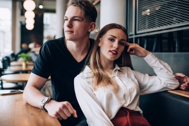 Siyah tişörtlü genç ve şık giyimli kadın. Kafasında el pozu olan kadın. Gün ışığında kafede oturuyor.