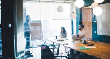 Büyük pencereli ve ofis malzemeleriyle konferans masalı çağdaş tasarım işyerindeki meslektaşlarına fikir sunan iş adamı