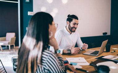 Ofis odasındaki toplantıda iş arkadaşlarıyla masaya otururken bilgisayarını kullanan neşeli sakallı bir yönetici.