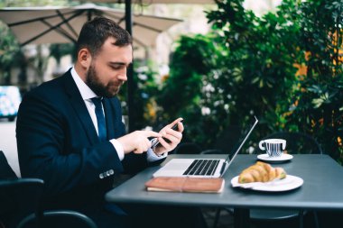 Kafkasyalı işadamının, sokak kafedeki serbest iş sırasında yaptığı akıllı telefon ihbarını kontrol etmesi, resmi olarak giyinmiş erkek girişimcinin mesajlaşma için cep telefonunda 4G kablosuz internet kullanması,