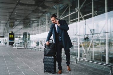 Beyaz iş adamı havaalanı terminalinin yanında bekliyor. Şirket ortağıyla uluslararası bir konuşma yapmak için cep telefonu kullanıyor. Resmi giyinmiş patron iş seyahatleri sırasında cep telefonuyla iletişim kuruyor.