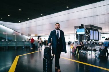 Resmi giyinmiş, valizli, seyahat çantalı, havaalanında yürüyen ve iş gezisinde poz veren gururlu CEO 'ya bakan şirket yöneticisinin tam boy portresi.