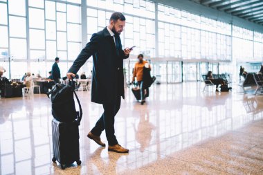 Genç işadamının cep telefonu aygıtını havaalanındaki kapı bilgilerini indirmek için kullanması, iş seyahatleri sırasında akıllı telefon uygulaması üzerinden kablosuz internet kullanması,