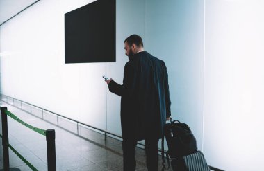 Akıllı telefonuyla bavul mesajı gönderen beyaz iş adamı seyahat reklamları için fotokopi alanı olan reklam duvarının yanında yürürken gururlu CEO cep telefonu bankacılığı ve bilet kesiyor.