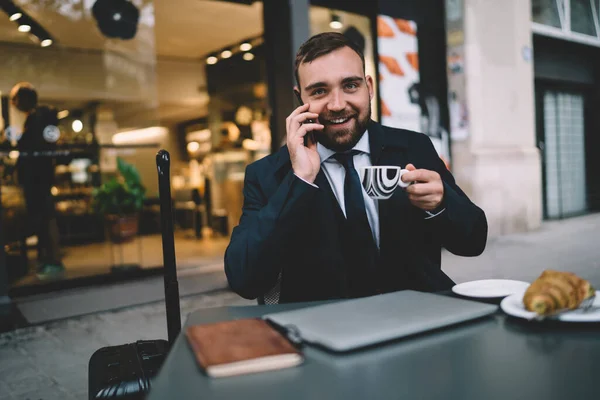 Positiv Skäggig Affärsman Med Kopp Kaffe Och Smartphone Ler Och — Stockfoto