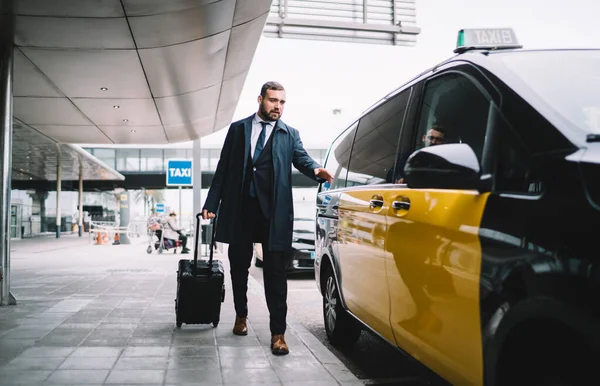 Handsome male passenger in formal outfit sitting in yellow cab getting to business meeting during travel trip, Caucasian man lawyer with baggage suitcase ordering taxi transport at airport exterior