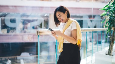 Çekici Asyalı bir kadın ticari merkezde dikilirken arka planı bulanık mesajlaşırken eğleniyor.