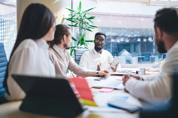 作業プロセスを議論する従業員の乗組員との会議テーブルに座って深刻な暗い肌の男の上司 プロの多人種の乗組員は プロジェクト戦略についてのアイデアや意見を共有します — ストック写真