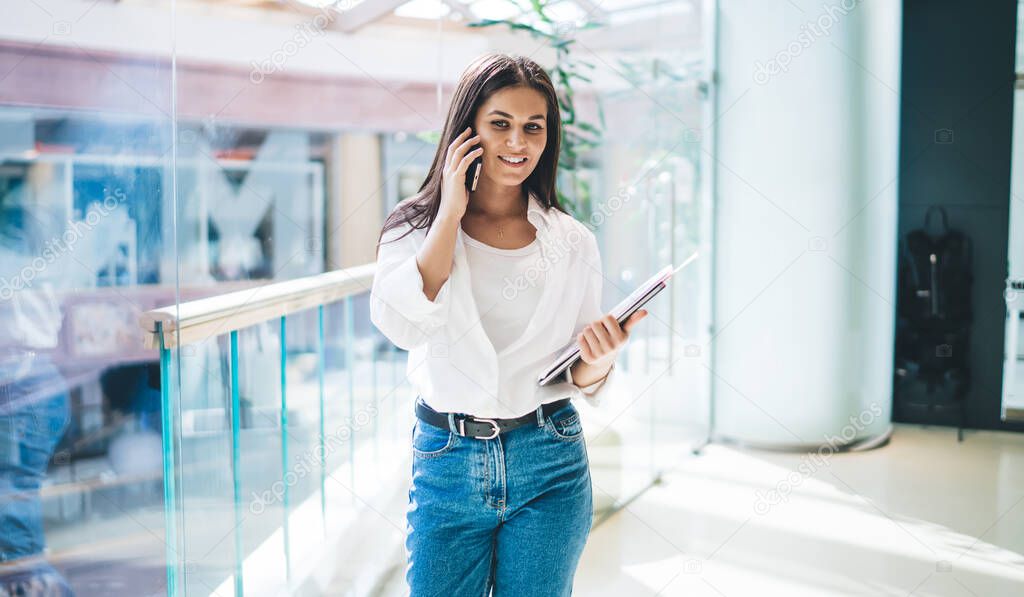 Successful female marketer in smart casual clothing using cellphone gadget for making friendly cellular call via technology application, confident woman enjoying mobility conversation in workspace