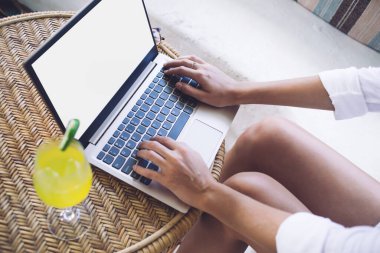 Yukarıdan gelen ekin boş ekranla internette sörf yaparken bir yandan da aydınlık odada bir bardak buzlu içecek ile masada oturuyor.