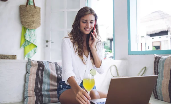 在现代阳光充足的房间里 穿着休闲装 头戴智能手机 头戴笔记本电脑 头戴果汁 坐在沙发上的快乐女性 — 图库照片