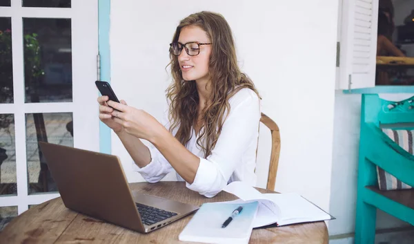 Mujer Encantadora Enfocada Gafas Blusa Blanca Sosteniendo Teléfono Inteligente Mientras —  Fotos de Stock