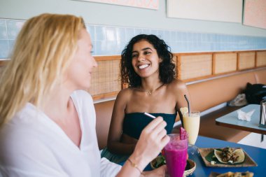 Meksika yemeği ve meyve kokteylleriyle canlı iletişimin keyfini çıkaran çok ırklı en iyi arkadaşlar. Lezzetli yemekleri ve bistro masasında oturan lezzetli yemekleri tartışan neşeli bayan kızlar.