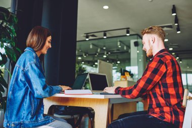 Birlikte çalışma alanındaki işbirliği sırasında web tasarımı oluşturan yetenekli işçilerin yan görünümü, beyaz erkek ve kadın online rezervasyon ve bankacılık yaparken dizüstü bilgisayarlarda kablosuz internet taraması yaparken