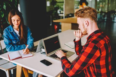 Beyaz tenli erkek ve kadın öğrenciler birlikte çalışma alanında bilgisayar ve not defteri kullanarak bir araya geldiler. İnternet sitesinden bilgi edinme konusunda yetenekli adamlar.