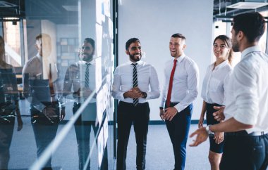 30 yaşındaki neşeli meslektaşlar modern çalışma ortamında dostça bir işbirliği içinde iş deneyimlerini tartışıyor, başarılı erkek ve kadın yönetici yöneticiler yatırım fikirleri üzerinde işbirliği yapıyorlar.