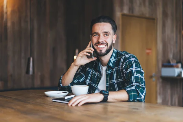 Usmívající Mladý Vousatý Muž Ležérním Oblečení Mluvící Smartphonu Zatímco Vzdáleně — Stock fotografie