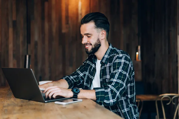 Autónomo Barbudo Positivo Con Camisa Cuadros Escribiendo Portátil Mientras Está — Foto de Stock