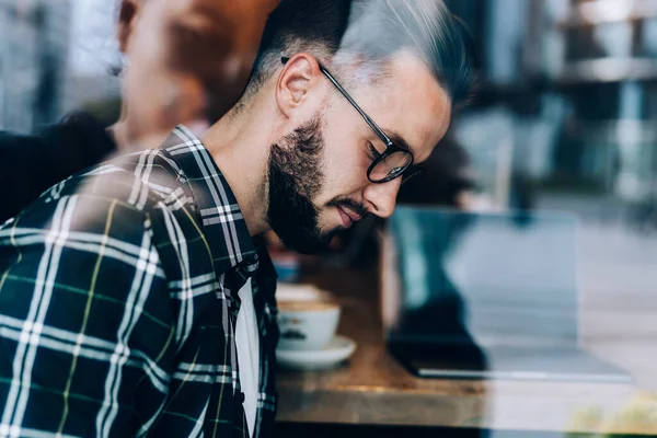 Door Glazen Zijaanzicht Van Een Bebaarde Jongeman Met Bril Zittend — Stockfoto