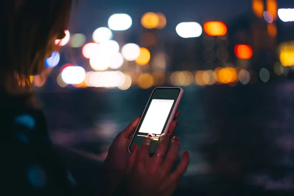 作物認識できない女性を使用してピンクの場合には現代的な電話でアプリケーションモックアップ暗い夜の川やボケ市のライトのぼやけた背景に — ストック写真