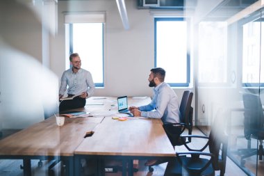 Gülümseyen beyaz iş ortakları yeni başlayan projede verimli bir işbirliğinin keyfini çıkarıyorlar, birbirleriyle konuşuyorlar, başarılı erkek girişimciler planlama ve başarılı çalışma sürecini tartışıyorlar.