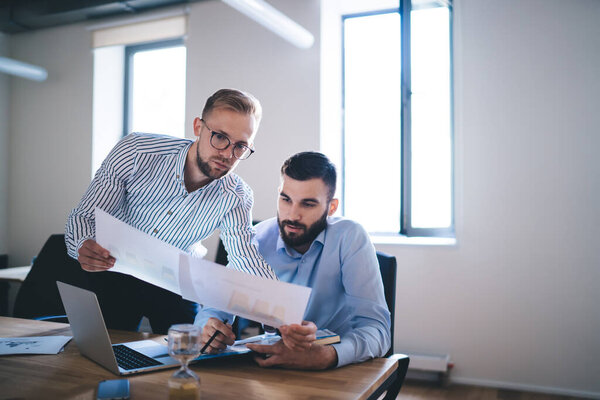 Professional male colleagues talking to each other cooperating on working project, Caucasian men entrepreneurs discussing planning and business strategies while brainstorming at table desktop